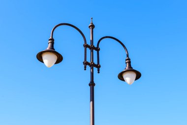 Güneşli bir günde mavi gökyüzüne karşı iki ampullü sokak lambası. Klasik tarzda çift lamba direği. Sokakları, parkları ve yolları aydınlatmak için modern enerji tasarrufu teknolojileri. Düşük açı görünümü.