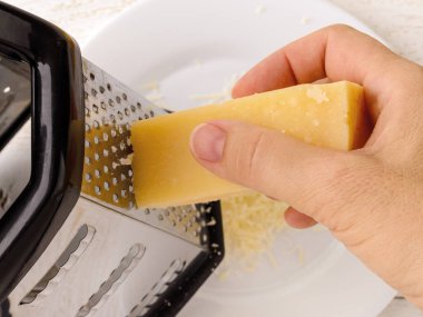 Kadın eli geleneksel İtalyan sert peyniri Grana Padano ya da parmesan peynirini beyaz tabakta rendeliyor. Pizza, sandviç, salata için lezzetli malzeme. Üst görünüm.