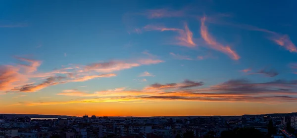 Panoramic shot of golden blue twilight sky with orange pink clouds over a small city. Scenic skyscape just after the sun goes down over the horizon. Beauty in nature.