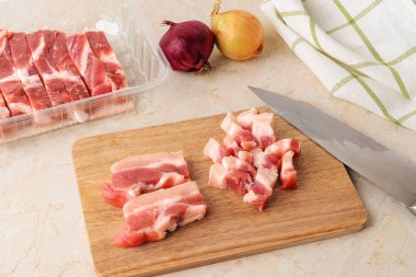 Mutfak masasında keskin bir bıçakla taze domuz göbeğini tahta kesme tahtasıyla küçük parçalara ayırmak. Tek kullanımlık şeffaf plastik bir yiyecek kabında et. Evde yemek pişir. Üst görünüm. 