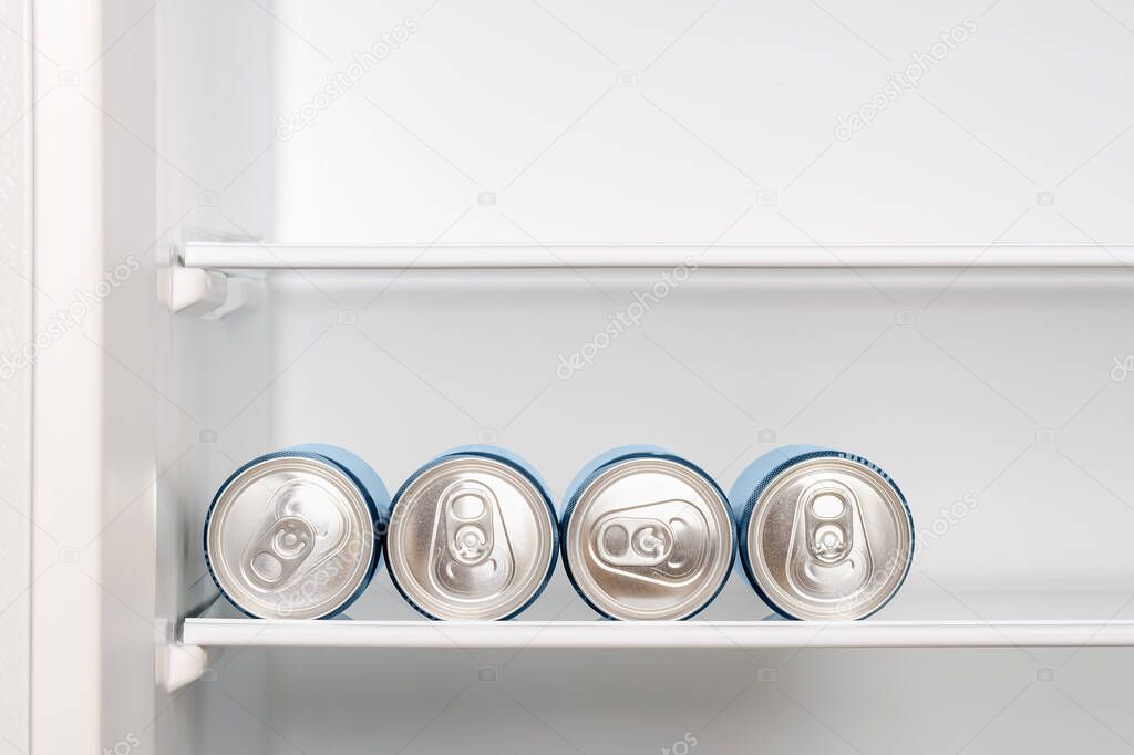 Four cans of beer or soda on the shelf in an empty home fridge. Cooling beverages in aluminum cans with pull tabs before drinking. Copy space. Front view.
