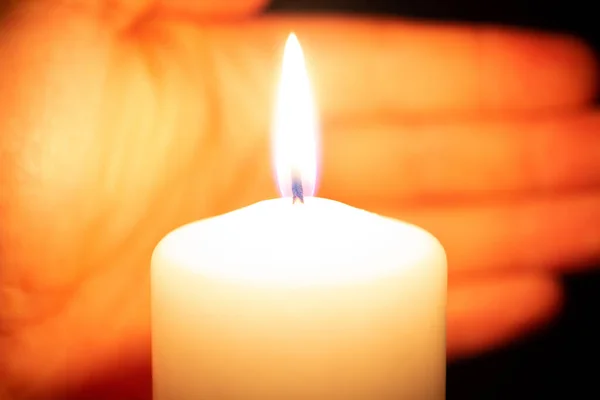 A big white burning candle with a hand in the background