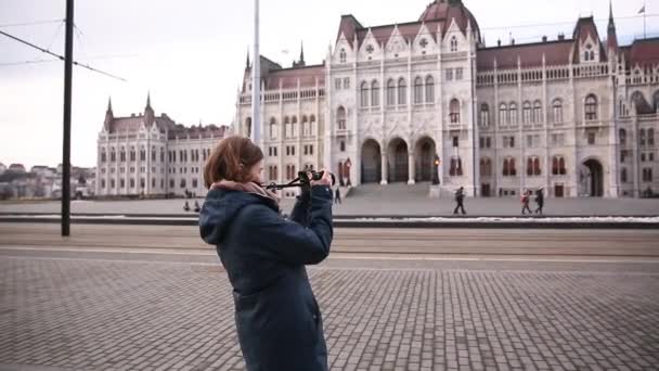 Tourist woman takes pictures near the Parliament in Budapest in autumn or winter — Stock Video