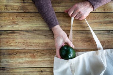 Yaşlı bir kadının elleri taze organik avokado ahşap arka plan üzerinde düz yatıyordu Eko alışveriş torbaya koy. Üstten görünüm. Ekoloji koruma kavramı