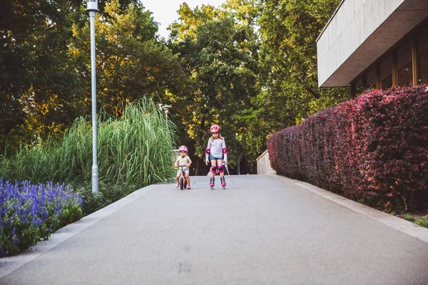 2人の小さな女の子がローラーに乗り 夏の公園でランバイク 安全な乗車のための保護パッドと安全ヘルメットを身に着けている子供たち 子供のためのアクティブな屋外スポーツ 兄弟は競争相手だ夏のスポーツ — ストック写真