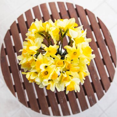 Açık ahşap bir masa üzerinde beyaz bir vazoda sarı nergis buket