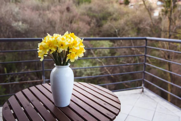 Bouquet of yellow daffodils in a white vase on a wooden table outdoor — Stock Photo, Image