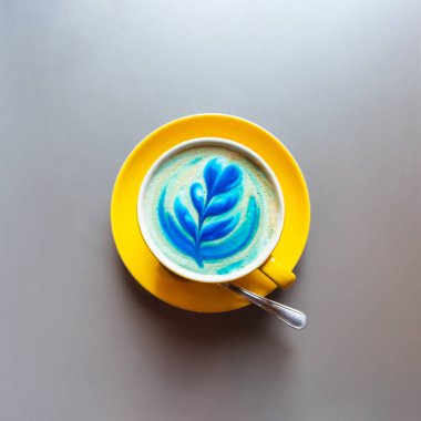 Gri ahşap masa arka plan üzerinde köpük üzerinde sanat çiçek yaprakları ile sarı sıcak trendy mavi latte Düz yatıyordu, latte sanat ile sağlıklı içecek, sabah taze kadar, closeup