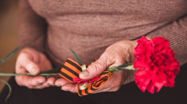 Mayıs 9 Rus tatil Zafer Bayramı kavramı arka plan. Yaşlı kadın elinde kırmızı bir karanfil tutan ve St. George's şerit. Yakın çekim. Tonda vintage. Afiş