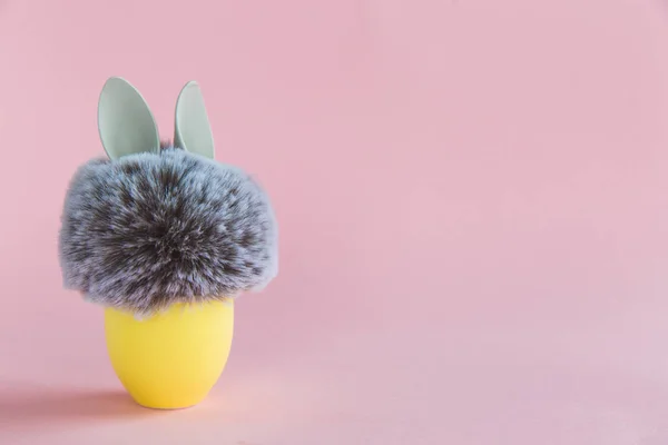 Pelota de piel con orejas de conejo de conejo en soporte de huevo amarillo sobre fondo brillante. Concepto mínimo de Pascua — Foto de Stock