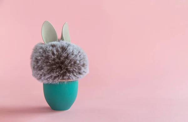 Pelota de piel con orejas de conejo en soporte de huevo aguamarina sobre fondo brillante. Concepto mínimo de Pascua — Foto de Stock