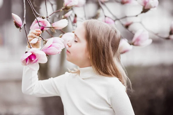 Mädchen 8-9 Jahre Portrait. hält einen Ast eines Magnolienbaums. der Baum blüht in großen rosa Blüten — Stockfoto