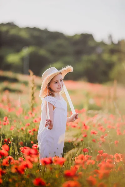 Little girl in a hat walks through a poppy field — Stock Photo, Image