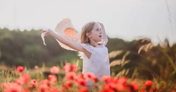 Ένα κοριτσάκι με καπέλο περπατάει σε ένα χωράφι με παπαρούνες. — Φωτογραφία Αρχείου