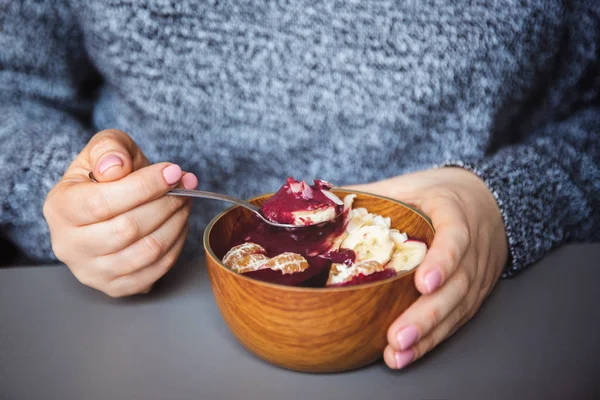 Acai smoothie, granola, tohumlar, gri masada kadın elinde ahşap bir kapta taze meyve. Sağlıklı kahvaltı kase yeme