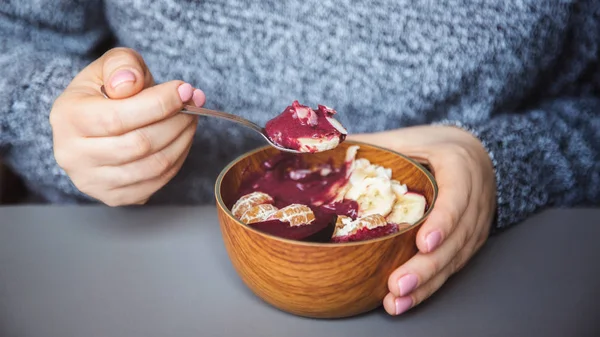 Acai smoothie, granola, tohumlar, gri masada kadın elinde ahşap bir kapta taze meyve. Sağlıklı kahvaltı kase yeme