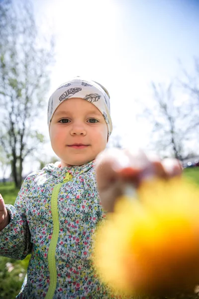 Kleines Mädchen sitzt auf dem Gras und hält gelben Löwenzahn — Stockfoto