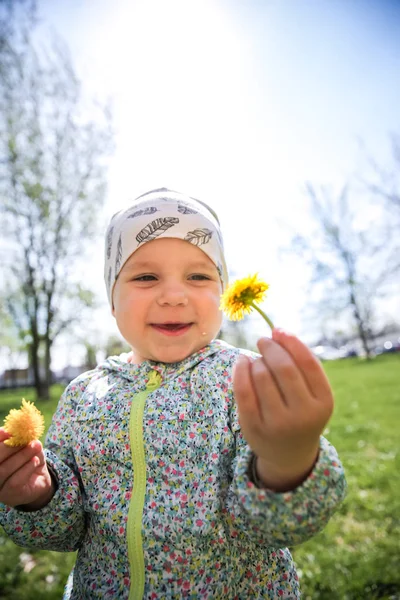 Kleines Mädchen sitzt auf dem Gras und hält gelben Löwenzahn — Stockfoto