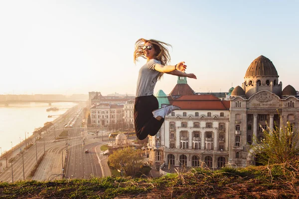Vacker kvinna hoppar mittemot berömda fasaden och ingången till Hotel Gellert på stranden av Donau i Budapest, Ungern — Stockfoto