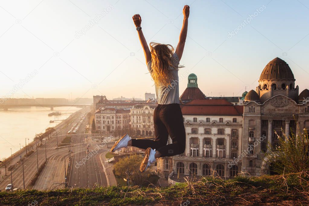 Beautiful woman jumping opposite famous facade and entrance to Hotel Gellert on banks of Danube in Budapest, Hungary