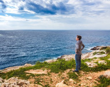 Adam uçurumun kenarında duruyor ve denize bakıyor