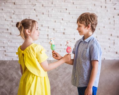 Sevimli kız ve erkek Paskalya gününde bir sopa üzerinde renkli el yapımı zencefilli tutan