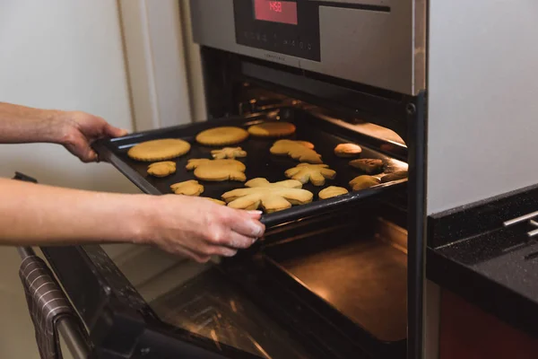 Вид сбоку женских рук, которые вытаскивают блюдо из духовки на кухне — стоковое фото