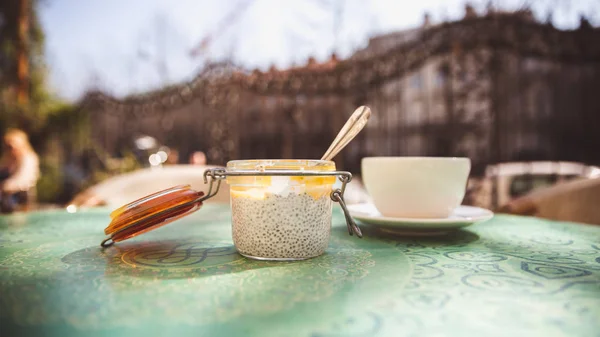 Copa de café y postre con semillas de chía en un frasco de vidrio sobre una mesa en un café al aire libre —  Fotos de Stock