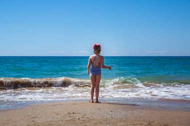 Kız güzel bir dalganın arka planında sahilde sırtı ile duruyor