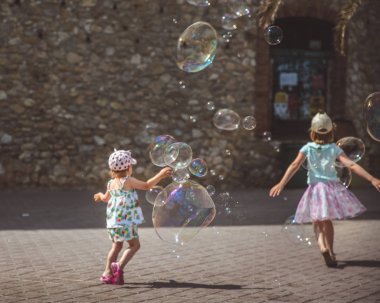 Büyük sabun kabarcıkları dışarıda havada uçar. Yaz günlerinde arka planda oynayan çocuklar