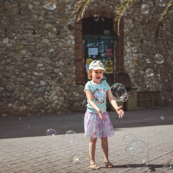 Mooi klein meisje speelt met grote bubbels in de straat in de zomerdag — Stockfoto