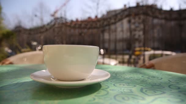 Taza de café caliente con vapor en la mesa en la cafetería por la mañana, al aire libre — Vídeo de stock