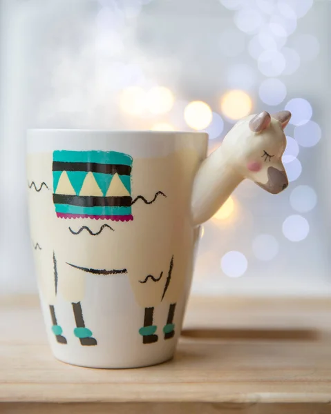 Hermosa taza de moda en forma de llama con té caliente con luces en el fondo — Foto de Stock