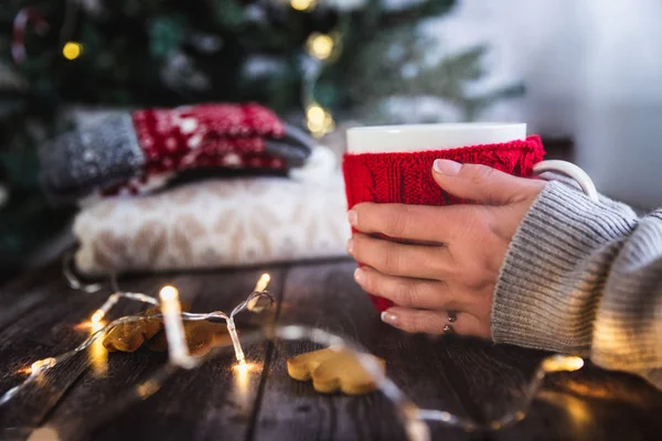 Frauenhände halten Weihnachtskaffee oder Teetasse mit Dampf, selbst gebackene Lebkuchen auf einem Holztisch, Süßspeisen, Weihnachtsbaum und Bokeh auf dem Hintergrund — Stockfoto