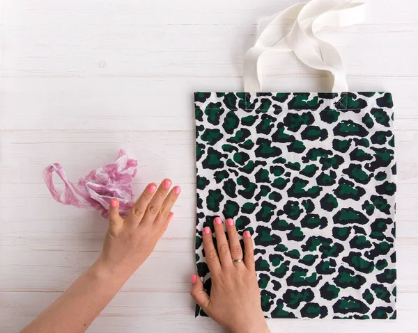 Womans hands choose eco shopping bag with trendy leopard pattern print against a plastic bag on white wooden background, Flat Lay. Save planet earth