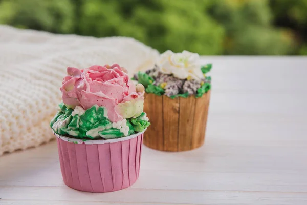 Két muffin, színes vaj virágok fehér fából készült asztal ragyogó zöldek háttérben — Stock Fotó