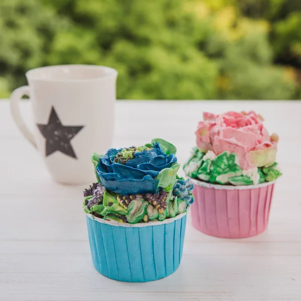 Két színes muffin, fehér csésze, csillag, fehér, fából készült asztal fényes zöldek háttér — Stock Fotó