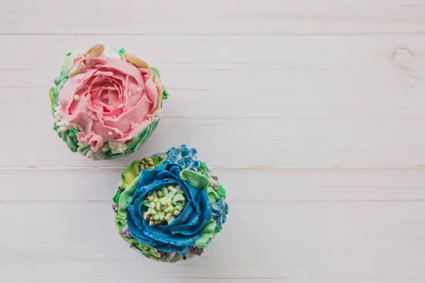 Két muffin, színes vajas virágok fehér fából készült háttér — Stock Fotó