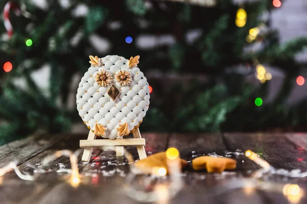 Hand painted Christmas gingerbread owl on a wooden stand with abstract bokeh background. Close-up.