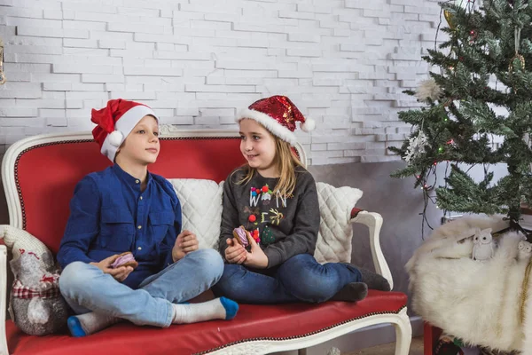 Счастливые милые маленькие дети в Санта-Клаусах едят вкусные кулинарные блюда дома — стоковое фото