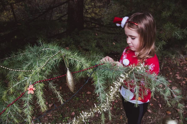 Merry Christmas and Happy Holidays. little girl decorating the Christmas tree outdoor in the yard of the house before holidays