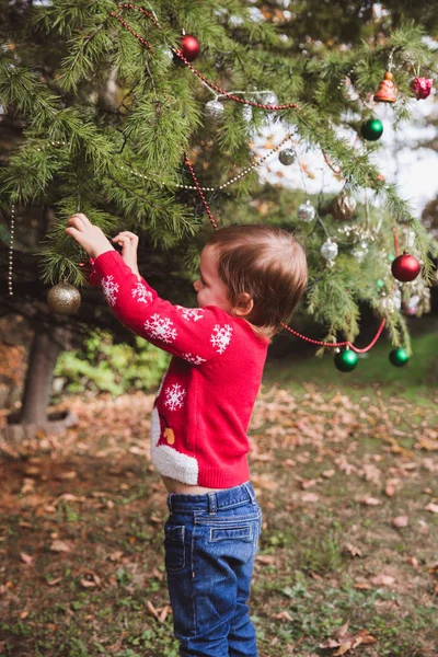 Merry Christmas and Happy Holidays. little girl decorating the Christmas tree outdoor in the yard of the house before holidays