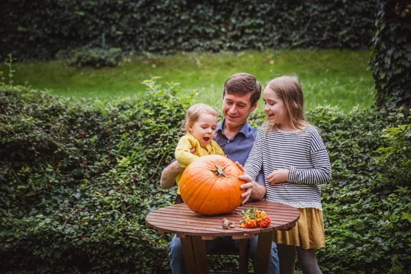 Feliz Dia das Bruxas. Pai e duas filhas olham para o rosto cortado na abóbora para o Halloween fora . — Fotografia de Stock