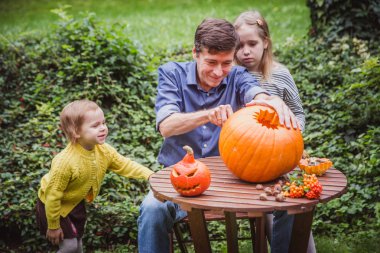 Happy halloween. Father and two daughter carving pumpkin for Halloween outside. Happy family clipart