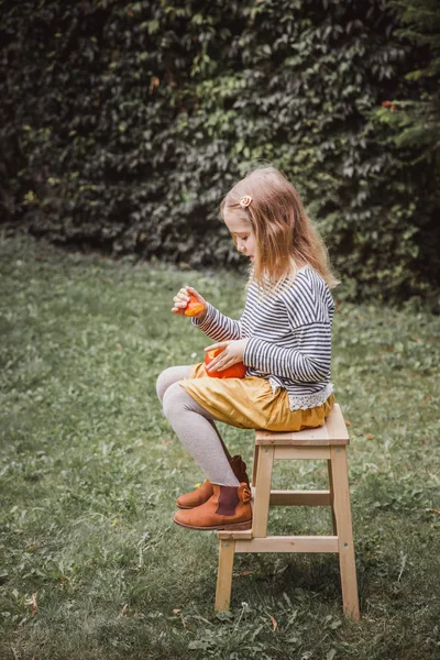 Boldog halloweent. Gyönyörű mosolygó kisgyermek ülések fa szék és birtokolja kis tök Jack O Lanterns szabadban. Vintage szűrőhatás — Stock Fotó