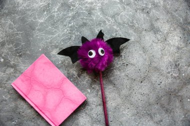 Gri arka plandaki notlar için modaya uygun mor yarasa kalem ve pembe defter. Cadılar Bayramı hala hayat. Düz yatıyordu