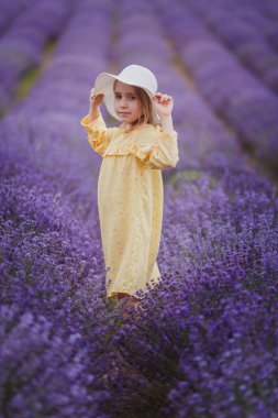 Sarı elbiseli gülümseyen küçük kız ve lavanta tarlasında koşan beyaz şapka