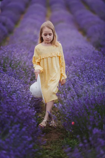 Lächelndes kleines Mädchen in gelbem Kleid und weißem Hut läuft in einem Lavendelfeld — Stockfoto