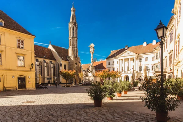 Sopron, Hungría - Octubre 2018: Estatua de la Trinidad y la Iglesia de la Cabra en el centro antiguo de Sopron, Hungría Imagen De Stock
