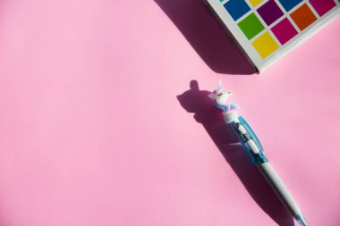 Notlar için renkli defter, pembe arka planda komik tek boynuzlu at kalemi. Düz yatıyordu. Üst Manzara. Boşluğu kopyala